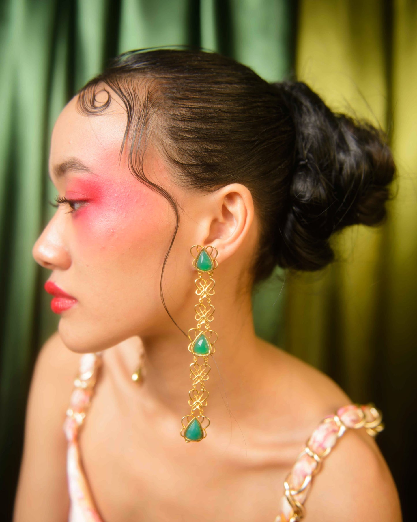A person wearing a sterling silver earring with natural stones, featuring a geometric design inspired by the endless knot of the eight auspicious signs of Buddhism.